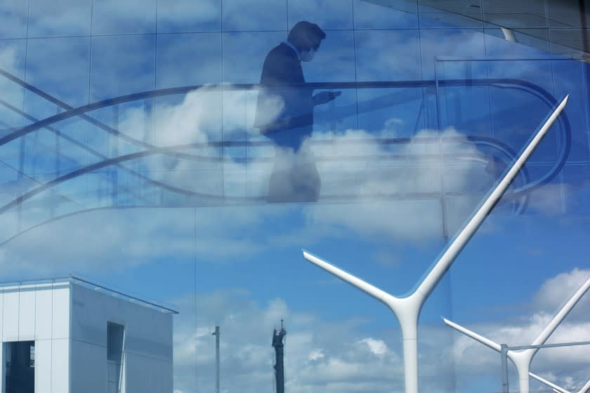 LOS ANGELES, CA - MARCH 24, 2020 - A traveler wearing a surgical mask rides the escalator to his flight as clouds are reflected in a nearby window at Los Angeles International Airport where the coronavirus has effected travel in Los Angeles on March 24, 2020. (Genaro Molina / Los Angeles Times)