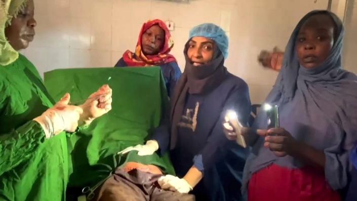 Dr Howaida Ahmed al-Hassan (second from right) speaks to the camera during a C-section as a woman illuminates the patient with light from cellphones