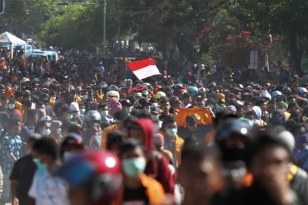 A protester raises the Indonesian flag while marching to the local parliament building during a protest in Kendari