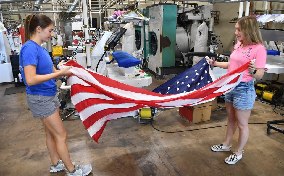 Ashlynn Hoff, left, and Kaylie Lange of Pressed Dry Cleaners fold a flag after cleaning. The company offers a free flag-cleaning service.