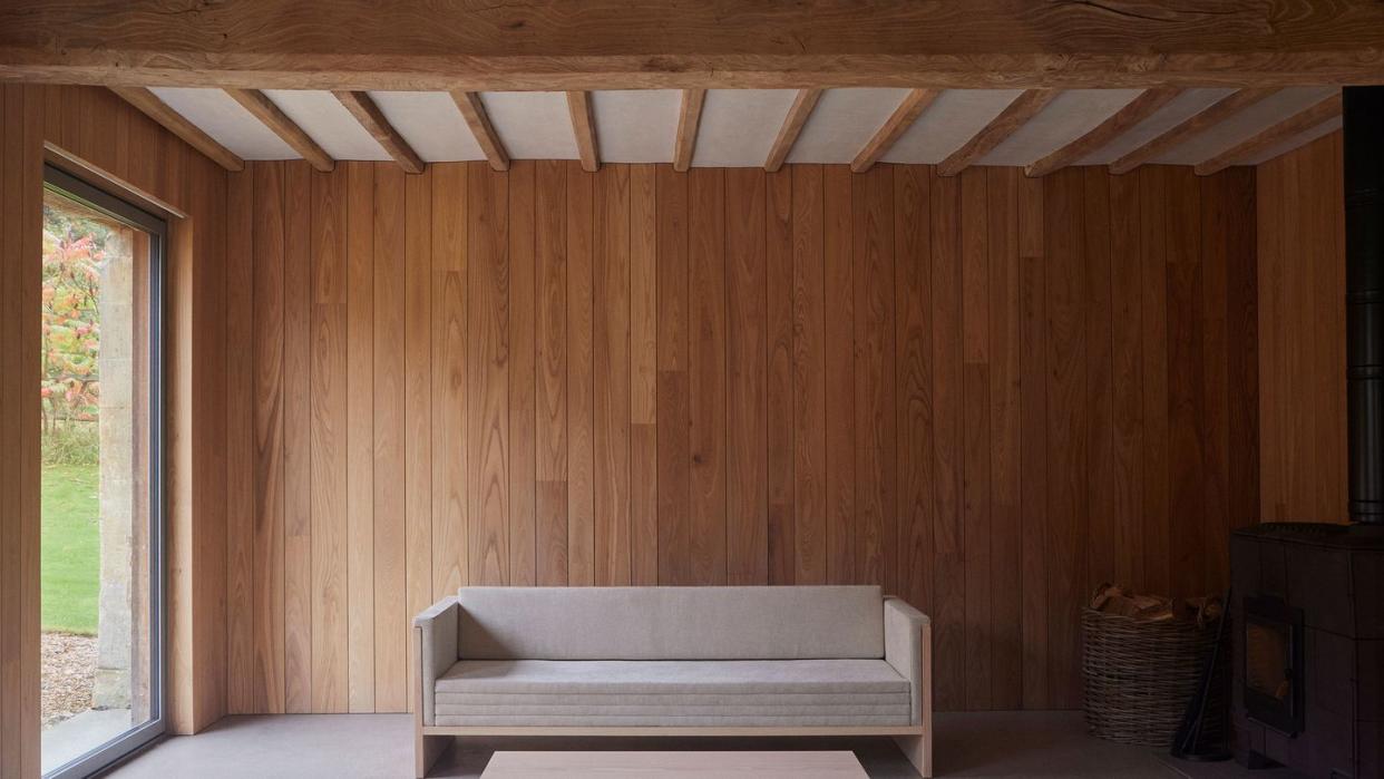 long wood daybed in simple elegant lines with velvet cushions and a simple matching cocktail table all against a panelled honey colored wall