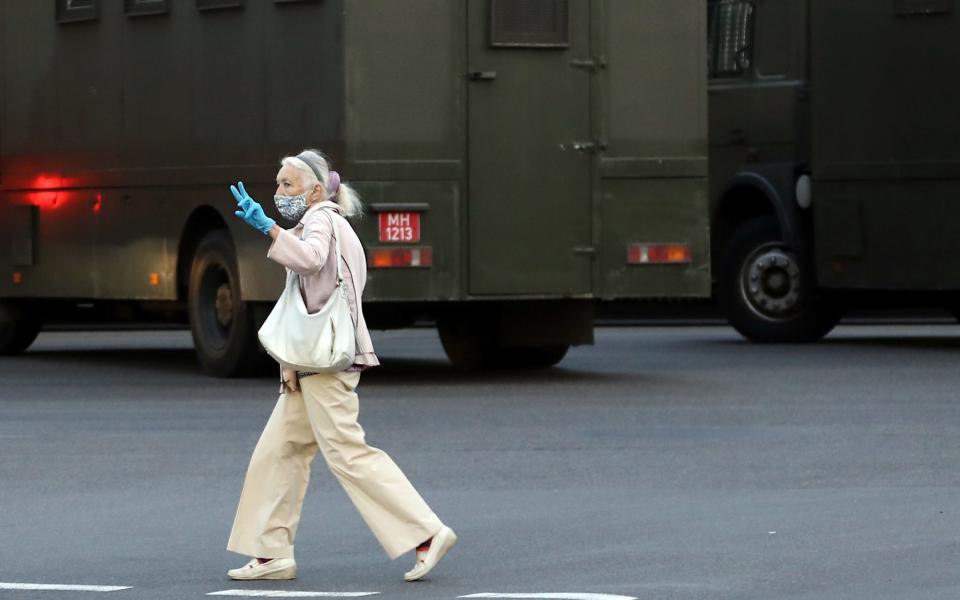 A woman flashes the V-sign near police vans in Minsk - TUT.BY/AFP via Getty Images