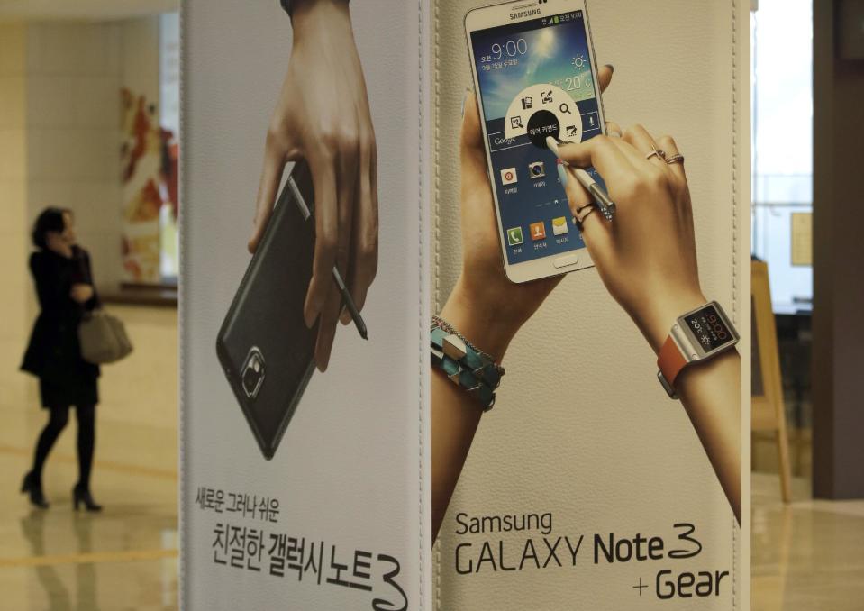 A woman uses her mobile phone near advertisements for Samsung Electronics' Galaxy Note 3 at a showroom of Samsung Electronics in Seoul, South Korea, Tuesday, Jan. 7, 2014. Samsung Electronics Co.'s fourth-quarter operating profit declined 6 percent over a year earlier, the company said Tuesday, underlining the challenges the world's largest smartphone maker faces as sales of mobile devices slow in advanced countries. (AP Photo/Lee Jin-man)