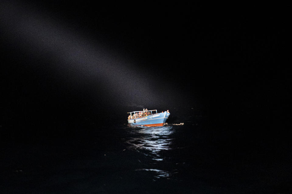 A spotlight shines on a small boat with migrants before they were rescued off the coast of Lampedusa on Tuesday Jan. 25, 2022. Seven migrants have died and some 280 have been rescued by the Italian Coast Guard after they were discovered in a packed wooden boat off the coast of the Italian island of Lampedusa. (AP Photo/Pau de la Calle)