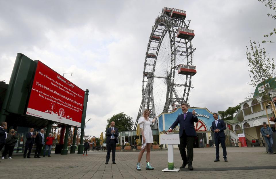 The Mayor of Vienna Michael Ludwig, center, presses a button to restarts the giant Ferris Wheel to symbolically signal the resumption of tourism in Austria in Vienna, Austria, Friday, May 29, 2020. Amusements are open again in Austria as part of relaxing the restrictions to slow the coronavirus and the COVID-19 disease. (AP Photo/Ronald Zak)