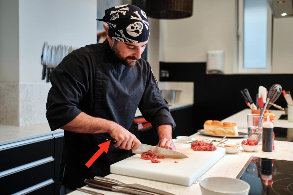 cook chopping meat and red arrow pointing to their uncovered hands