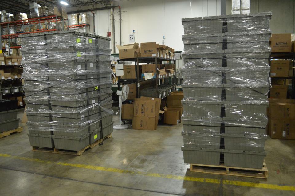 36 grey plastic bins sit in a warehouse in two stacks wrapped in plastic.