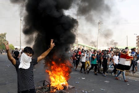 A demonstrator gestures as he stands close to burning tires blocking a road, during a protest over unemployment, corruption and poor public services, in Baghdad