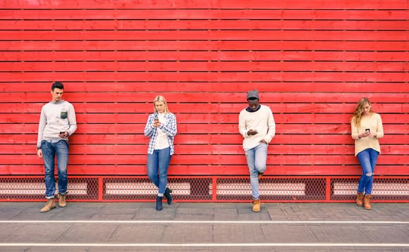 Four young people using their smartphones standing against a red wall.