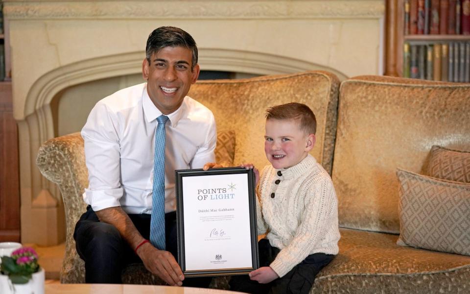 Rishi Sunak presents six-year-old Daithi Mac Gabhann, who is awaiting a heart transplant, with an award recognising "outstanding volunteers" for his contribution to his community - Niall Carson/PA