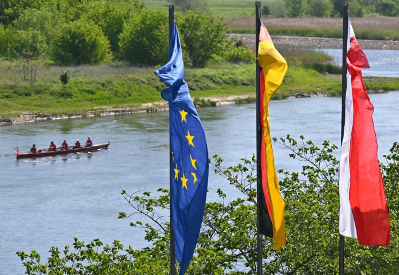 (LR) The flag of the European Union, the national flags of Germany and Poland blow in the wind on the banks of the German-Polish border river Oder on the 20th anniversary of Poland's accession to the EU.  Patrick Pleul/dpa