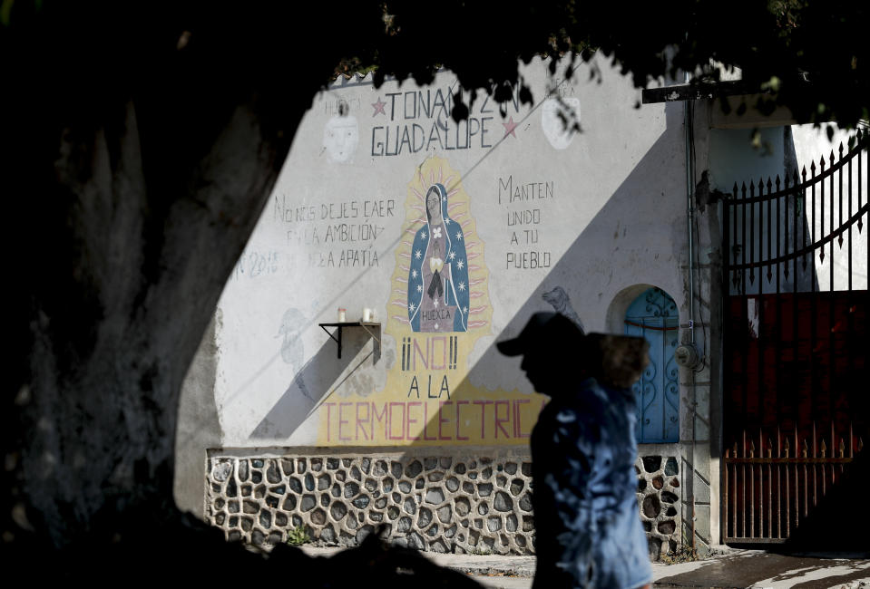 A man walks past an image of the Virgin of Guadalupe mural with text that reads in Spanish "No to the Thermo electric" in Huexca, Morelos state, Mexico, Saturday, Feb. 22, 2020. The the mural refers to a power plant that is part of a mega-energy project that includes a natural gas pipeline that traverses three states. It's at the heart of a years-long, contentious battle that calls into question the commitments of the new leftist government to indigenous land rights. (AP Photo/Eduardo Verdugo)