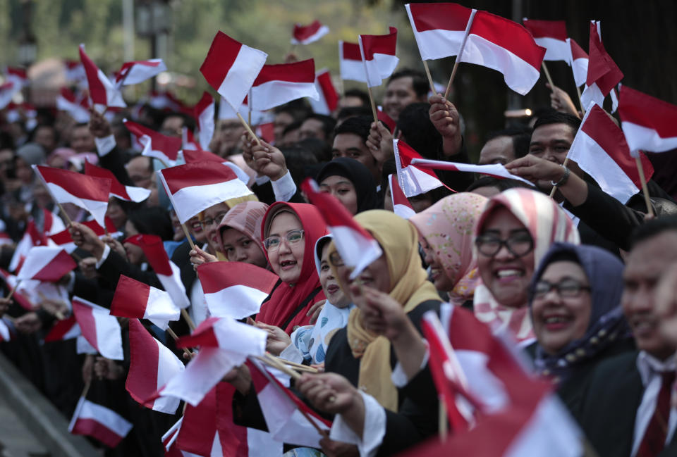 Palace staff wave Indonesian flags as the motorcade carrying President Joko Widodo leaves Merdeka Palace for the parliament building for his inauguration ceremony in Jakarta, Indonesia, Sunday, Oct. 20, 2019. The country's popular president who rose from poverty and pledged to champion democracy, fight entrenched corruption and modernize the world's most populous Muslim-majority nation is to be sworn in for his final five-year term with a pledge to take bolder actions. (AP Photo/Dita Alangkara)