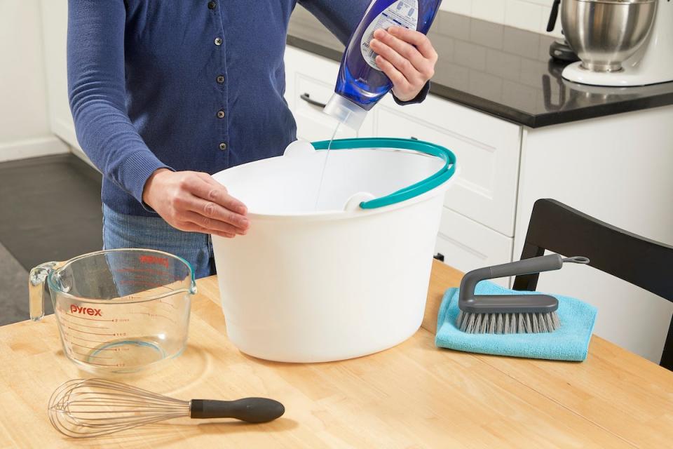 Woman mixing dish soap into a bucket of water to make upholstery cleaner.