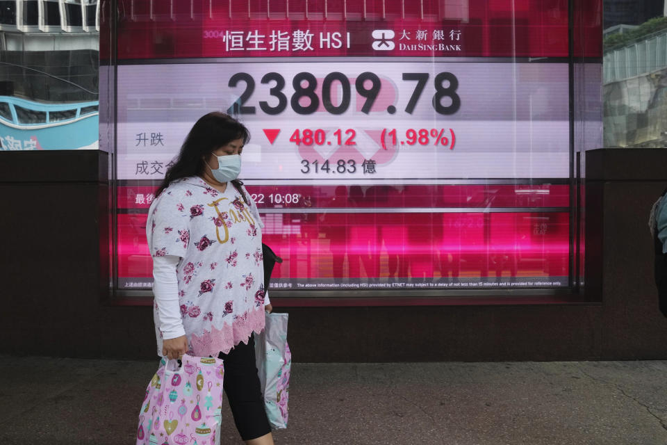 A woman wearing a face mask walks past a bank's electronic board showing the Hong Kong share index in Hong Kong, Thursday, Jan. 27, 2022. Asian stock markets tumbled by unusually wide margins Thursday after the Federal Reserve indicated it plans to start raising interest rates soon to cool inflation. (AP Photo/Kin Cheung)