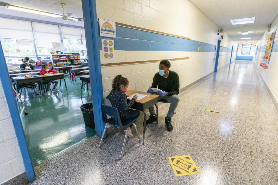 A teacher's assistant helps a first grade student with her work during the coronavirus outbreak in the hallway of School 16, Tuesday, Oct. 20, 2020, in Yonkers, N.Y. (AP Photo/Mary Altaffer)