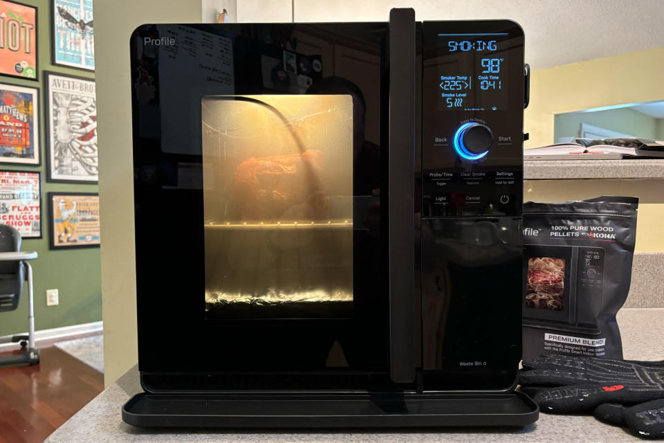 <p>GE Profile Smart Indoor Smoker from the front with the interior light on, sitting on a kitchen counter. A pork butt is being smoked inside.</p>
