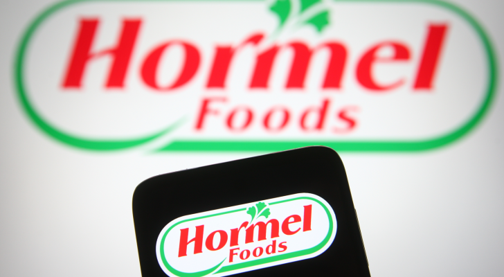 Hormel Foods Logo shown on a laptop screen behind a phone screen also showing the logo. HRL stock.