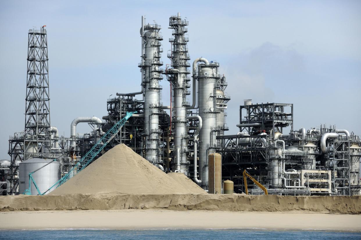 A chemical refinery stands behind a stockpile of sand to be used as landfill on Jurong Island in Singapore, on Thursday, March 1, 2012.  Photographer: Munshi Ahmed/Bloomberg