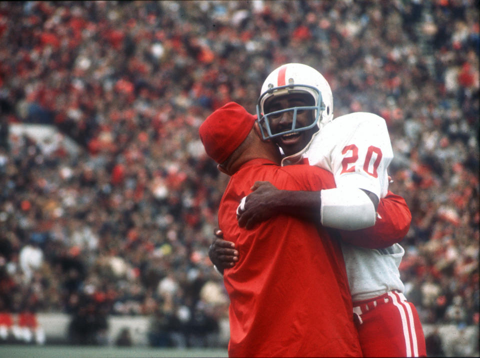 FILE - In this Nov. 25, 1971, file photo, Nebraska's Johnny Rodgers (20) hugs an assistant coach on the sideline after his punt return for a touchdown against Oklahoma in the first quarter of college football game in Norman, Okla., on Thanksgiving Day. The game on Thanksgiving 50 years ago is back in the spotlight as Nebraska and Oklahoma renew their rivalry on Saturday, Sept. 18, 2021. (Lincoln Journal Star via AP, File)