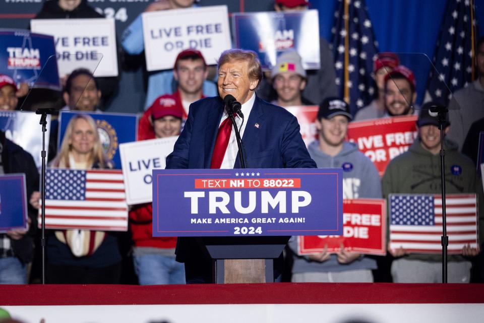 Donald Trump at a campaign rally, with an audience behind him.