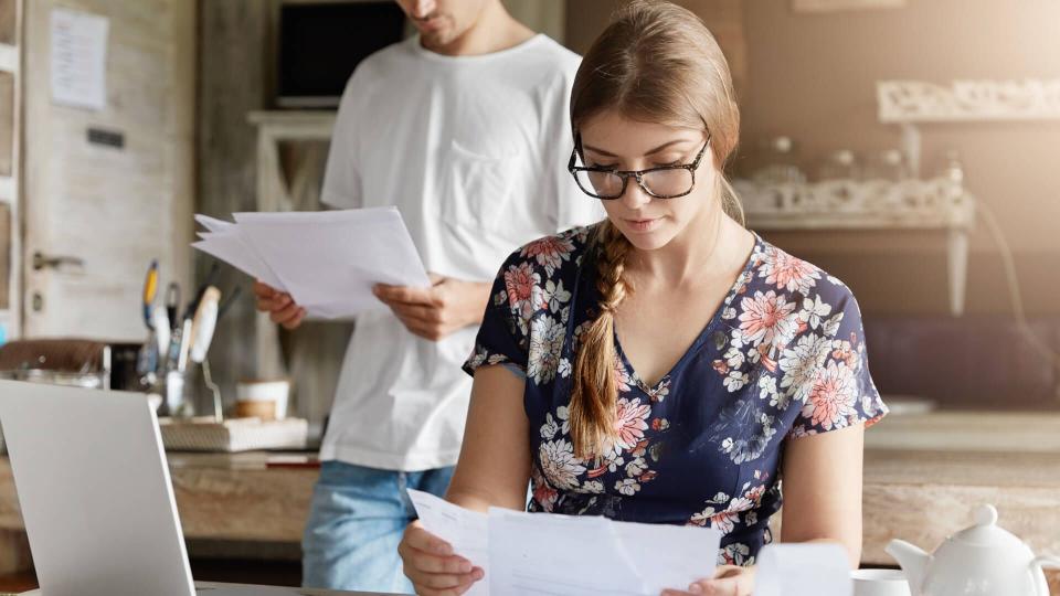 Beautiful woman reads documents attentively, prepares financial report, calculates figures and works on generic portable laptop computer.