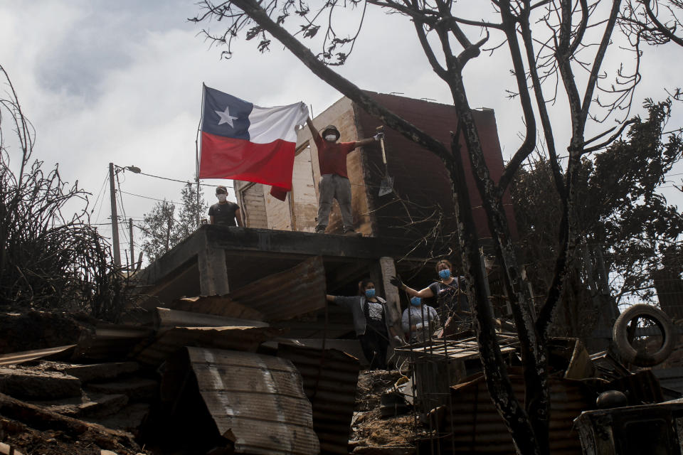 A resident poses displays a Chilean flag from a burnt-out house after forest fires reached his neighborhood in Vina del Mar, Chile, Sunday, Feb. 4, 2024. (AP Photo/Cristobal Basaure)
