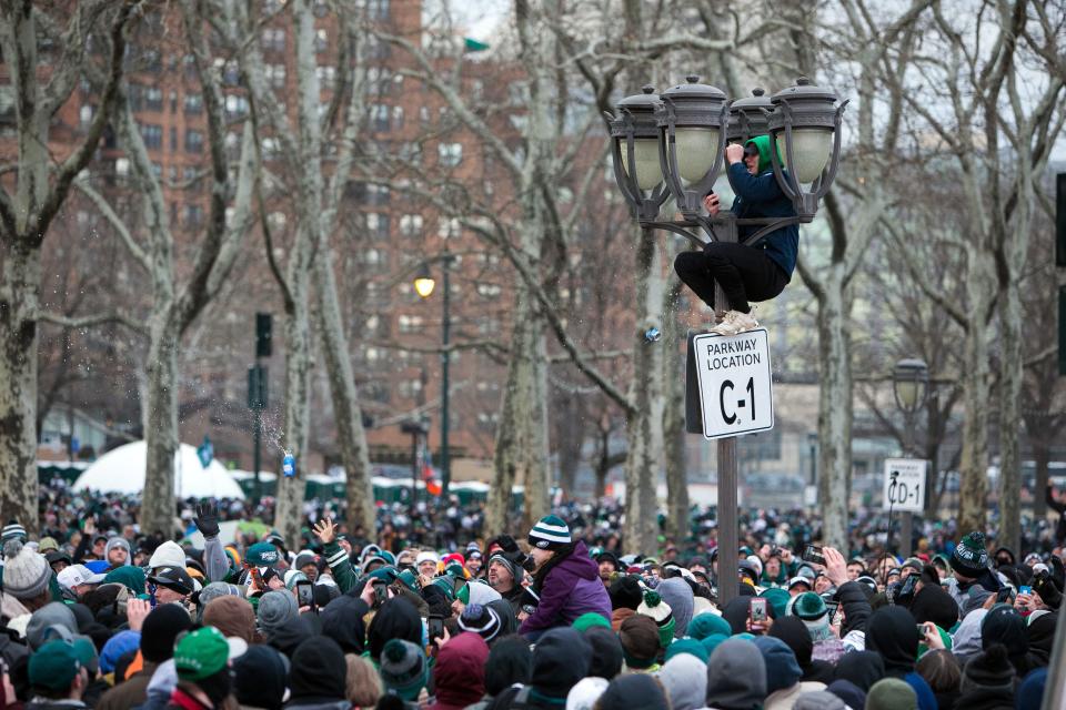 An Eagles fan climbs a light pole while others throw beer cans at him as thousands gather around the Rocky steps of the Philadelphia Museum of Art.