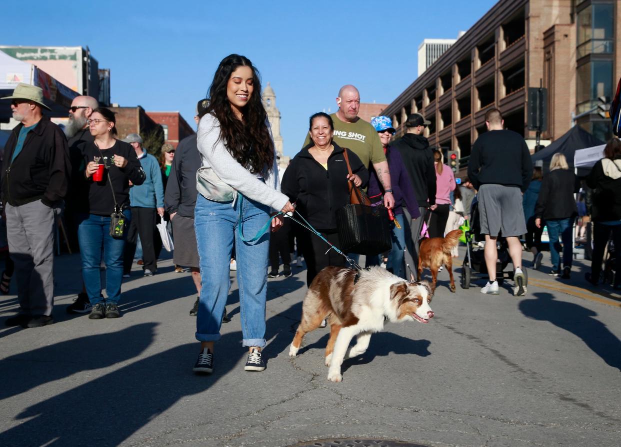 Katie Cartagena of Des Moines walks her dog, Coco, along Court Avenue during the opening day of the 2022 Downtown Des Moines Farmers' Market.