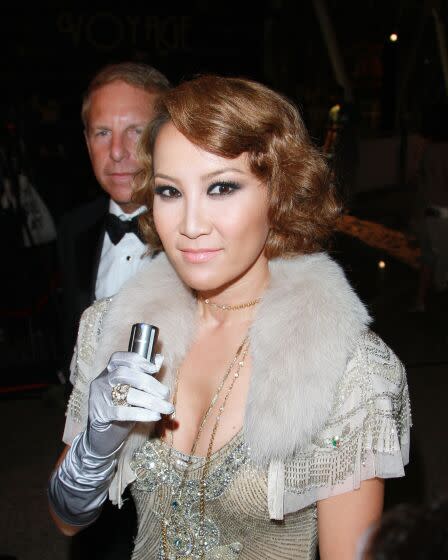 Coco Lee Man wears a silver and gold beaded dress with silver satin gloves, and her husband Bruce Rockowitz wears a tuxedo.