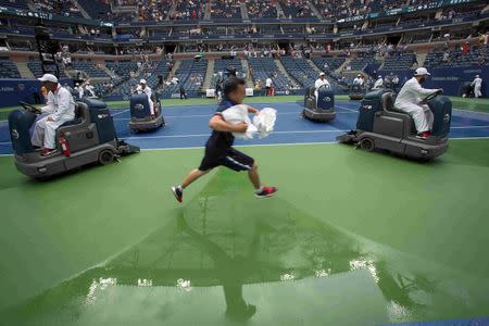 A ball boy jumps over the wet surface as workers dry the court after quarterfinals play between Simona Halep of Romania and Victoria Azarenka of Belarus was suspended due to weather at the U.S. Open Championships tennis tournament in New York, September 9, 2015. REUTERS/Carlo Allegri