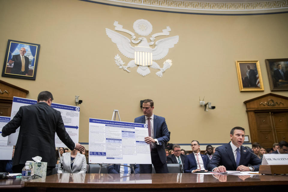 Aids set up posters as Acting Secretary of Homeland Security Kevin McAleenan, right, speaks at a House Committee on Oversight and Reform hearing on Capitol Hill in Washington, Thursday, July 18, 2019. (AP Photo/Andrew Harnik)
