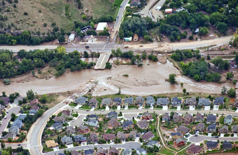 An aerial view shows flood waters and a washed-out road adjacent a suburban neighborhood in Lyons