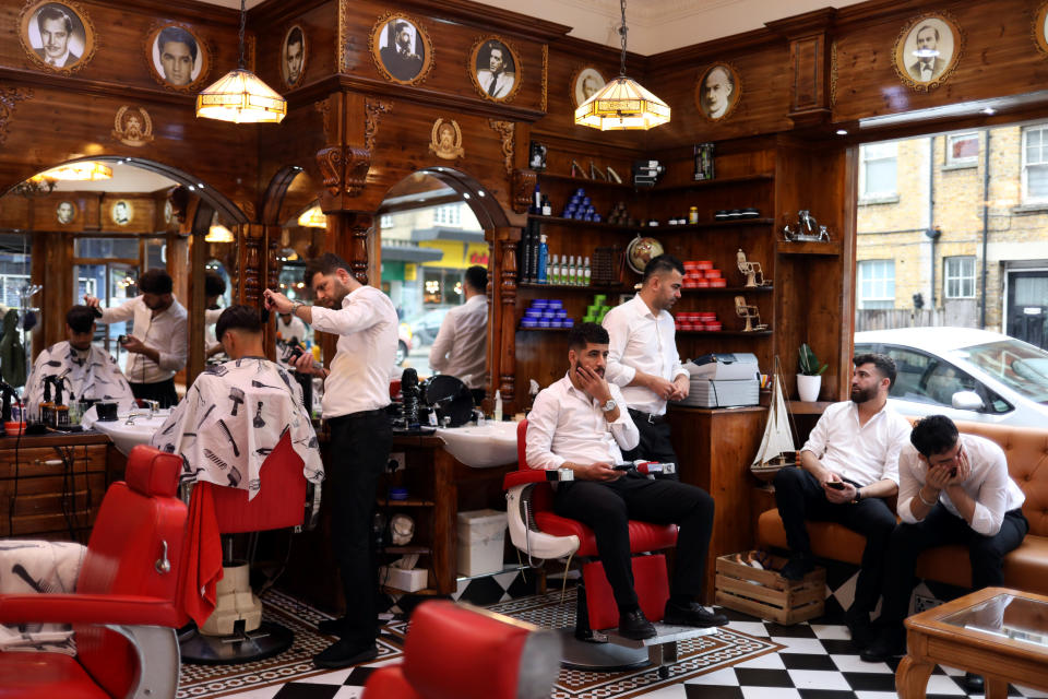 Un hombre se corta el pelo en una barbería de Streatham mientras otros clientes esperan a ser atendidos. (Foto: Hannah McKay / Reuters).