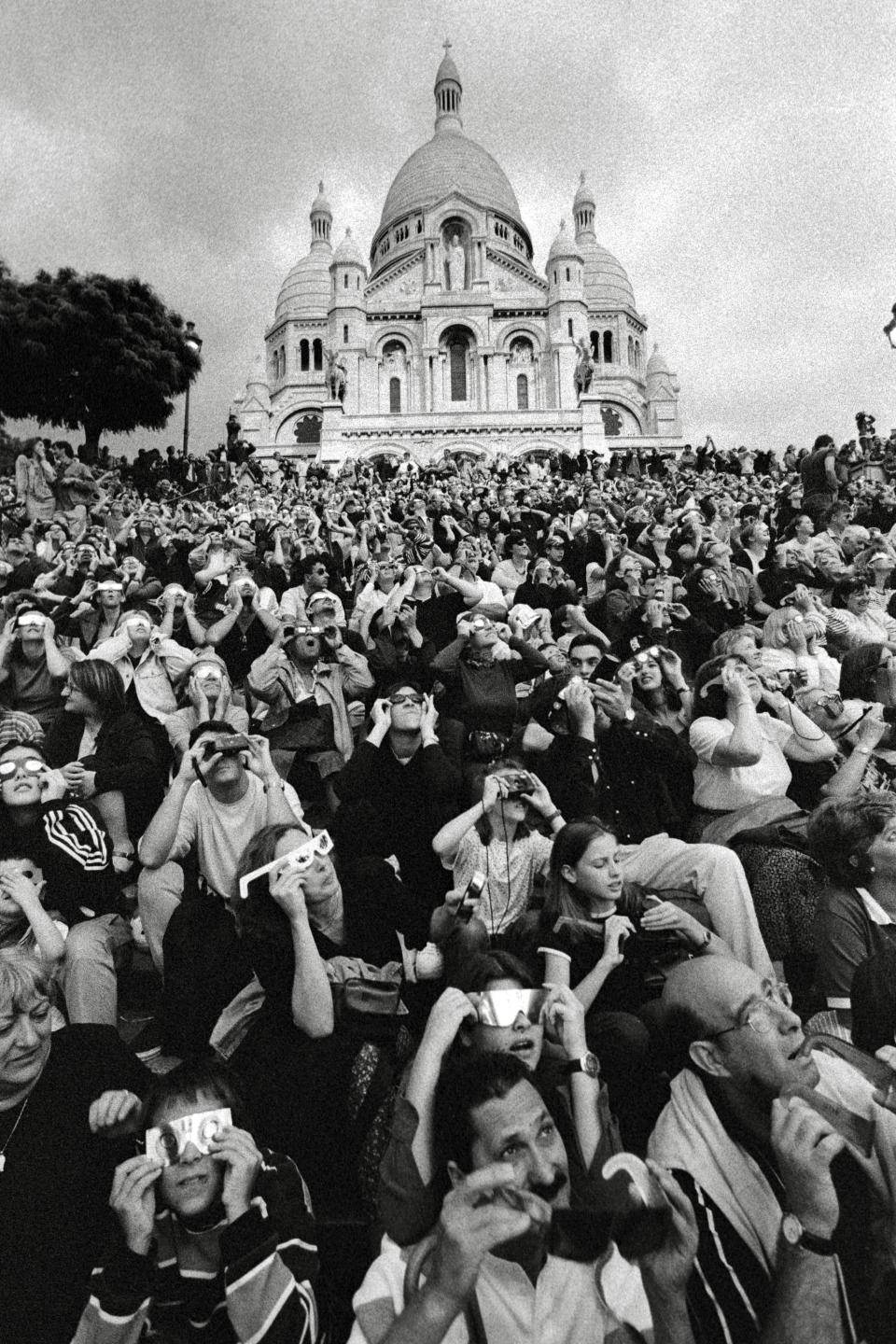 Black and white photo of many people looking at the solar eclipse in front of a dome-like structure.