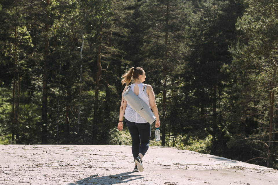 A woman from behind walking in nature carrying a yoga mat