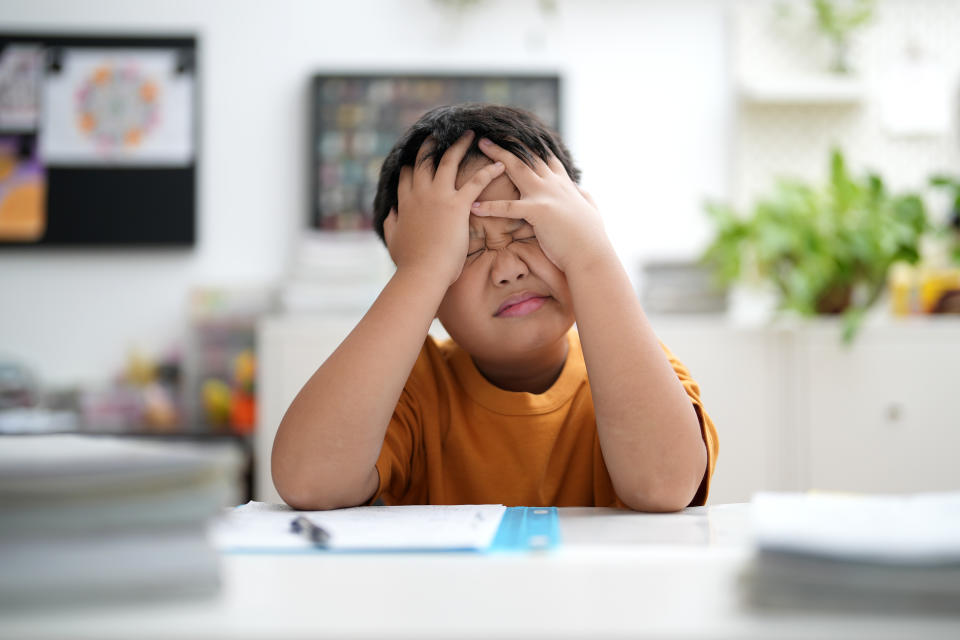 Young Asian boy is tired of doing homework, sitting at the table.