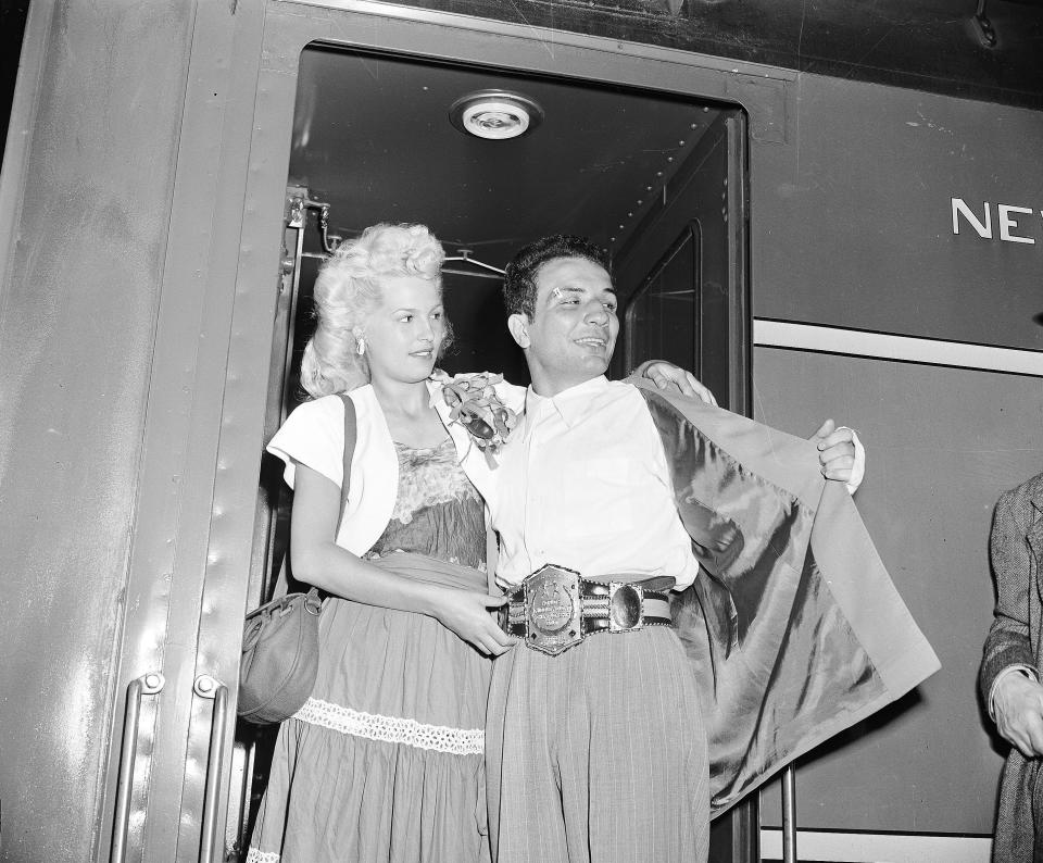 FILE - In this June 18, 1949, file photo, newly crowned World Middleweight Boxing Champion Jake LaMotta, shows off his championship belt as he arrives with his wife, Vicky, at New York's Grand Central Terminal from Detroit where he defeated French World Champion Marcel Cerdan. The movie "Raging Bull," about the life of Jake Lamotta, was No. 7 in The Associated Press’ Top 25 favorite sports movies poll. (AP Photo/File)