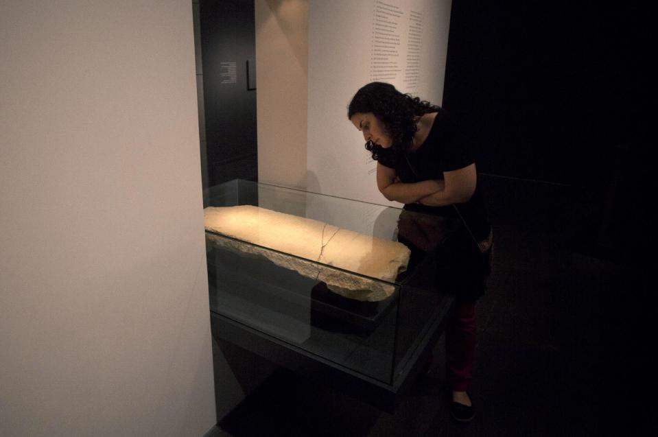 A museum worker looks at the "Gabriel Stone" as it is displayed at the Israel Museum in Jerusalem, Tuesday, April 30, 2013. An ancient stone with mysterious Hebrew writing and featuring the archangel Gabriel is being displayed in Israel--even as scholars continue to argue about what the inscription means. (AP Photo/Sebastian Scheiner)