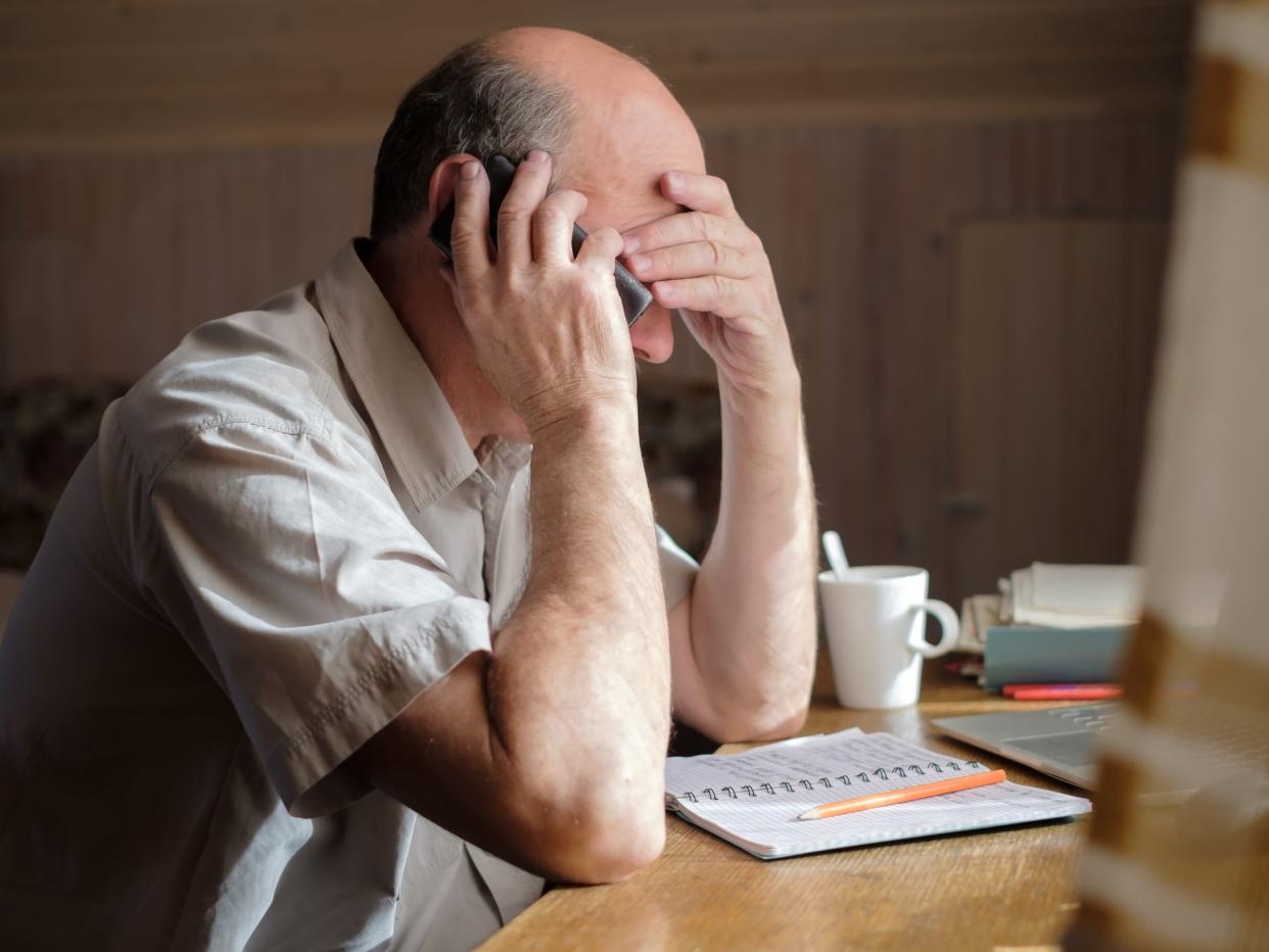 Senior man feeling upset having phone conversation depressed by hearing bad news sitting at home