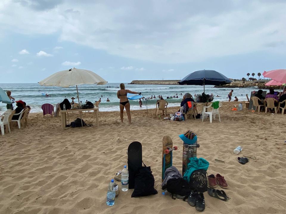 A crowded beach with skateboards stuck in the sand surrounded by umbrellas and people.