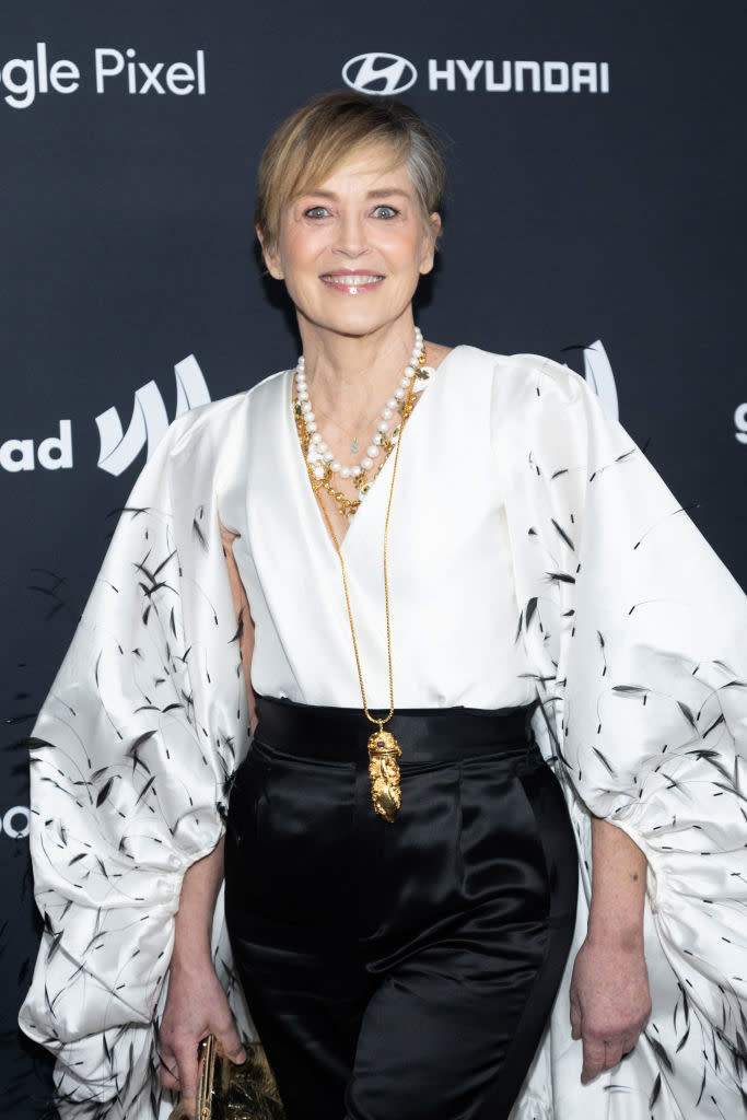 Sharon in elegant attire with draped sleeves and a necklace posing at an event