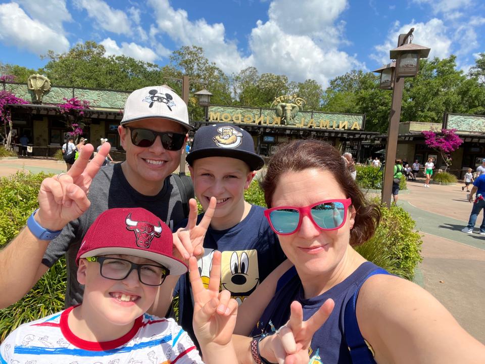 kari and her family posing holding up two fingers at the entrance to animal kingdom in dinsey world
