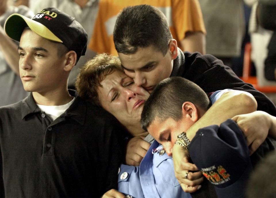 FILE - In this Friday, Sept. 21, 2001 file photo, Carol Gies, center, a wife of a missing firefighter, leans on son Ronnie as she is consoled by sons Bobbie, right, and Tommy, behind, during the ceremonies for the victims of the World Trade Center prior to the New York Mets game against the Atlanta Braves at Shea Stadium in New York. (AP Photo/Bill Kostroun, File)