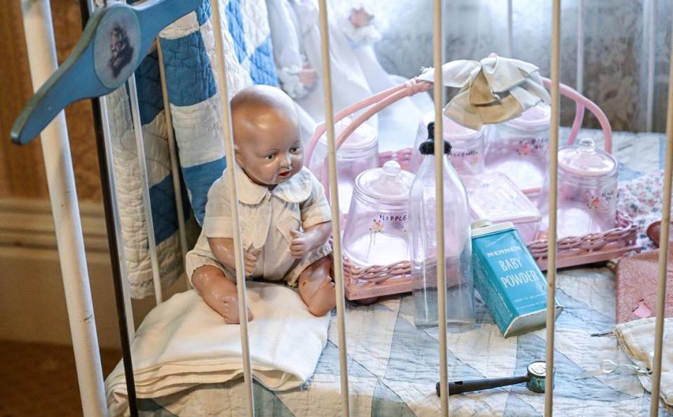 A baby doll sits in a crib with items used during Victorian times. The crib is said to have been used as recently as the 1990s.