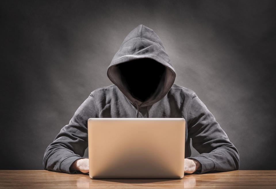 A mysterious hooded man whose face is in black using a computer.