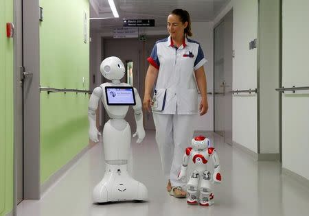 A nurse walks with "Pepper" (L) and "Zora" the robots, humanoid robots designed to welcome and take care of visitors and patients, at AZ Damiaan hospital in Ostend, Belgium June 16, 2016. REUTERS/Francois Lenoir