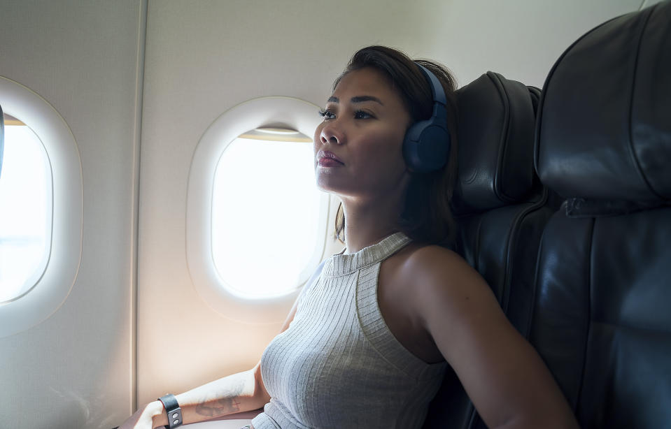 Woman in headphones looks out airplane window, contemplating, seated in cabin