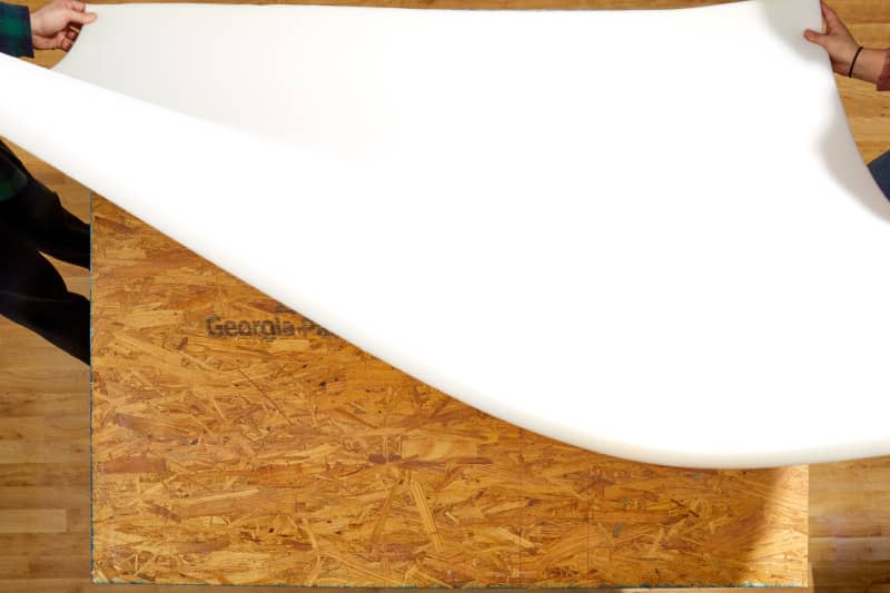 Overhead shot of two people laying the foam layer on top of the cut plywood.