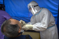 A worker wearing a protective suit swabs a man's throat for a coronavirus test at a community health clinic in Beijing, Sunday, June 28, 2020. China reported more than a dozen of new confirmed cases of COVID-19 on Sunday, all but a few of them from domestic transmission in Beijing, which has seen a recent spike in coronavirus infections. But authorities in the Chinese capital say a campaign to conduct tests on employees at hair and beauty salons across the city has found no positive cases so far, in a further sign that the recent outbreak has been largely brought under control. (AP Photo/Mark Schiefelbein)